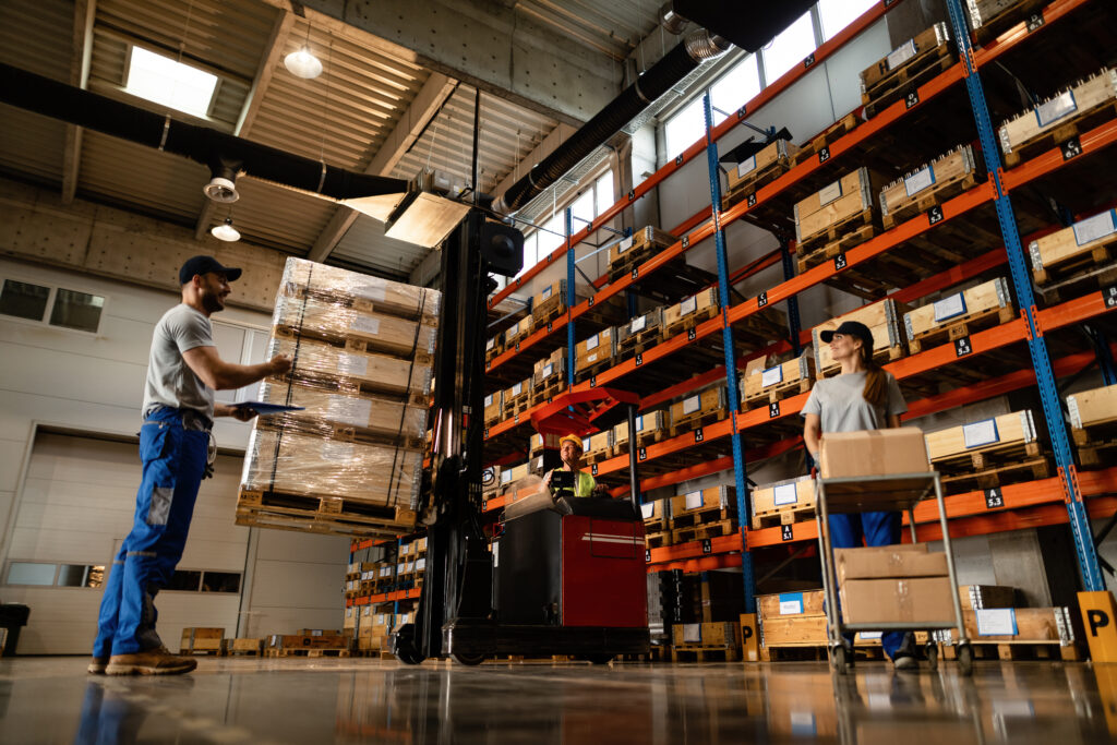 Low angle view of happy warehouse workers communicating while working with shipment in industrial storage compartment.